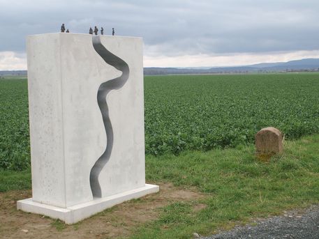 Grenzweg Kunst Der Verlauf des Harzer Grenzweges in eine Steinskulptur gearbeitet. Diese steht vor einem Feld.